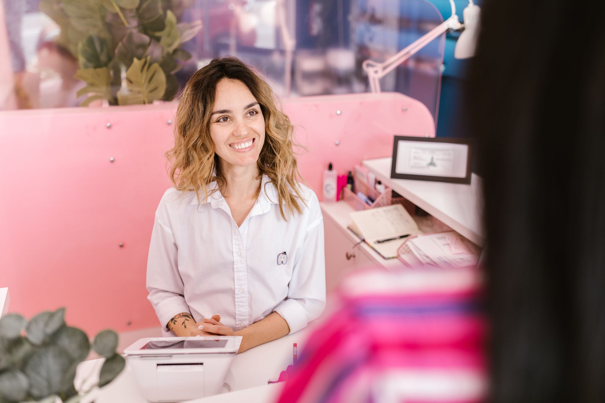 Recepcionista sorrindo no balcão do salão, com o tablet da agenda à frente, atendendo uma cliente