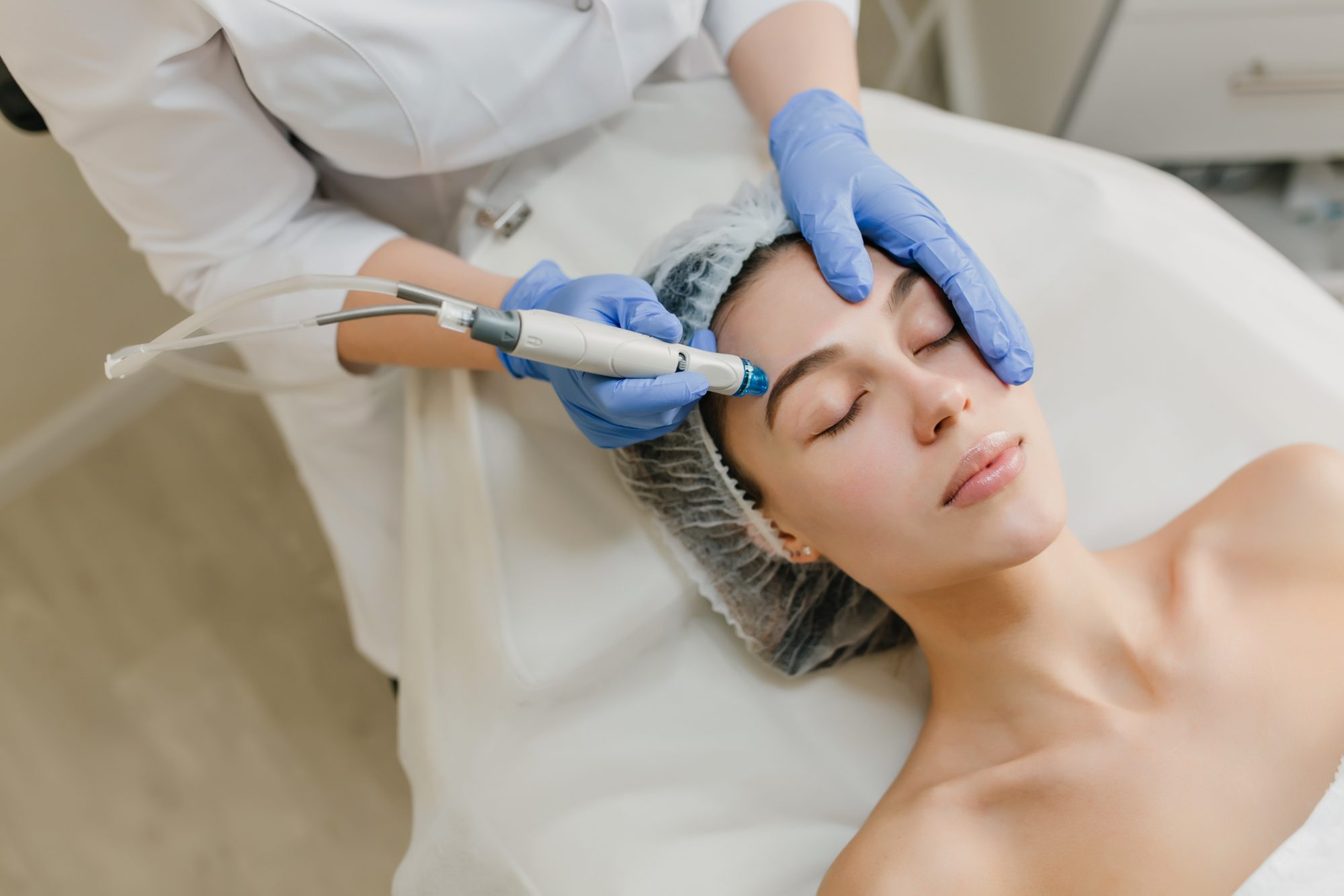 Esteticista de luvas fazendo um procedimento facial com aparelho em uma cliente deitada na maca