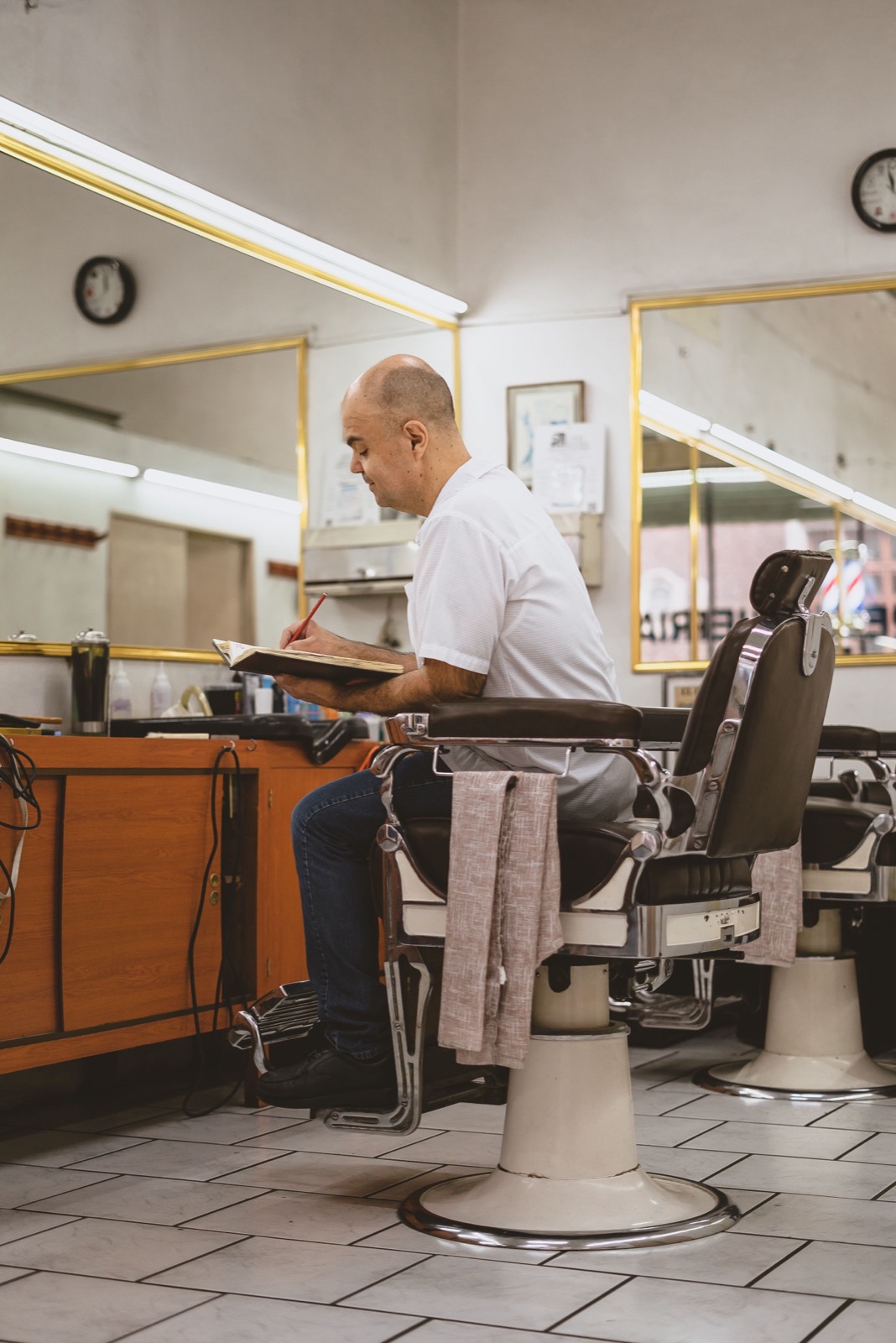 Dono de barbearia fazendo anotações num caderno, sentado na cadeira com o salão vazio