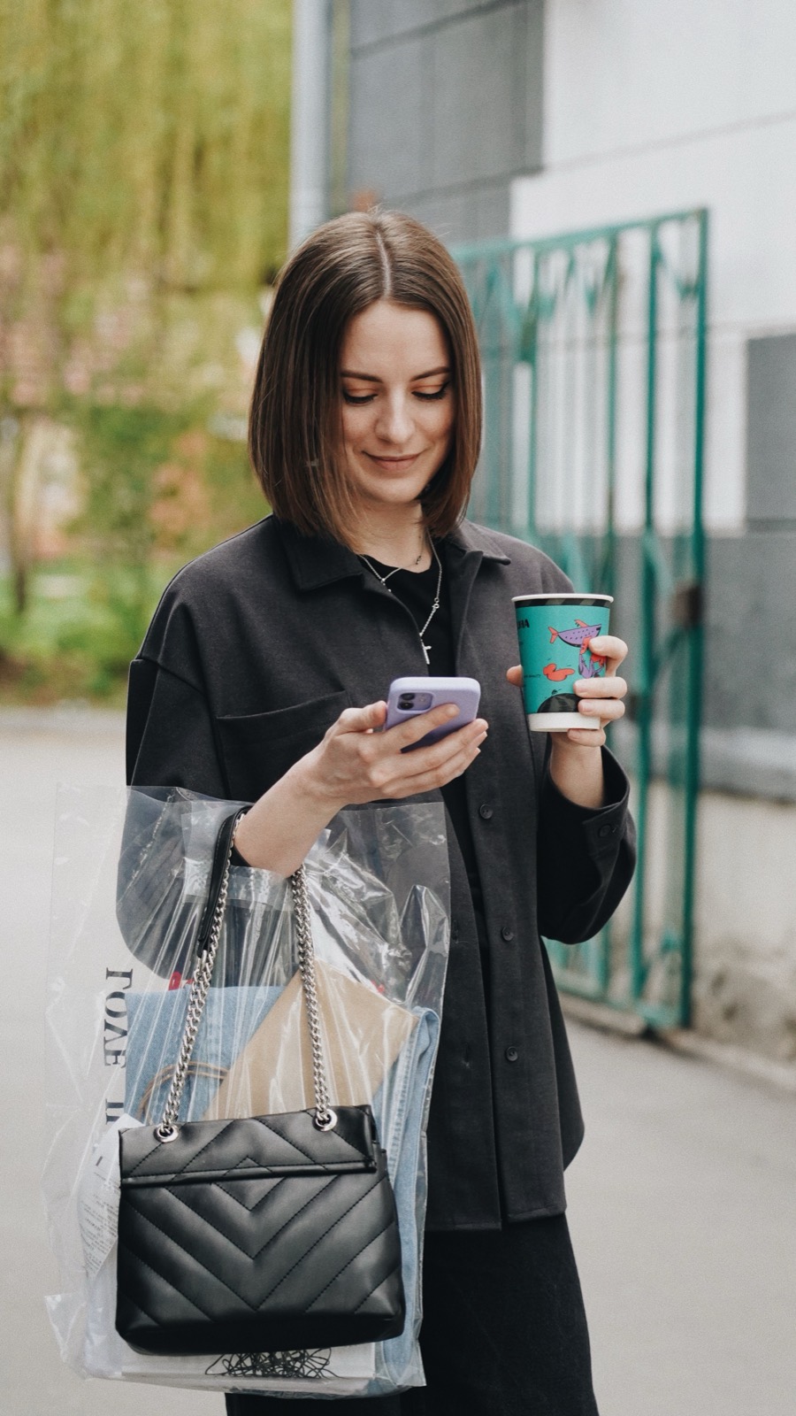 Mulher na rua, com café e bolsa, olhando uma notificação no celular