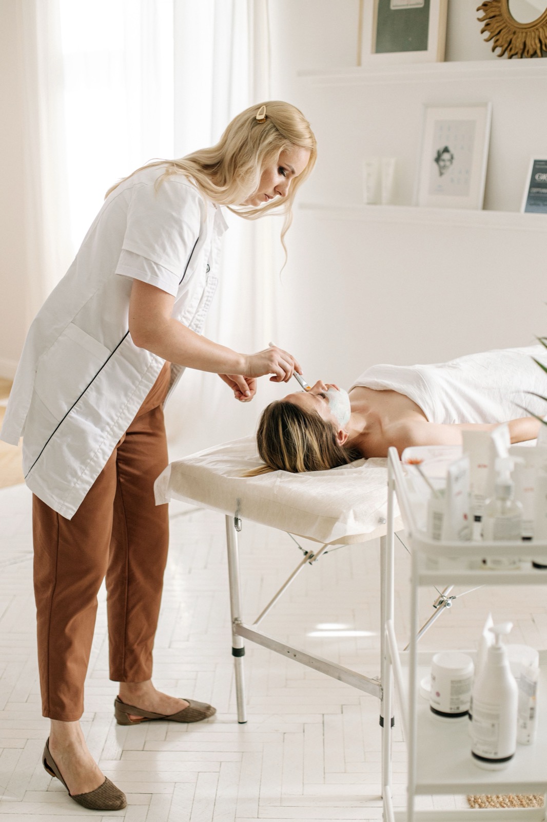 Esteticista fazendo um tratamento facial numa cliente deitada na maca, em ambiente claro