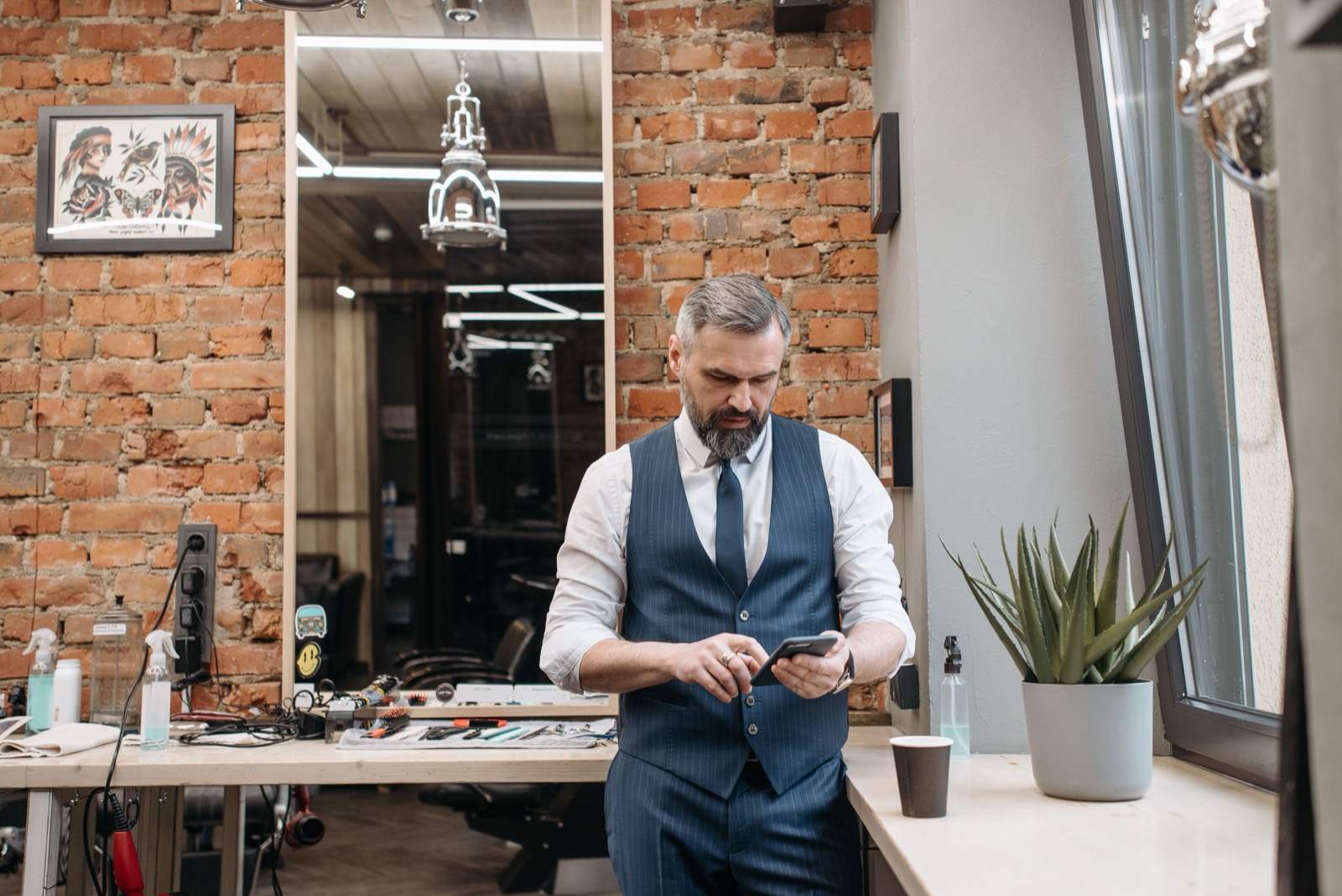 Gerente de barbearia, de colete, olhando o celular no meio do salão